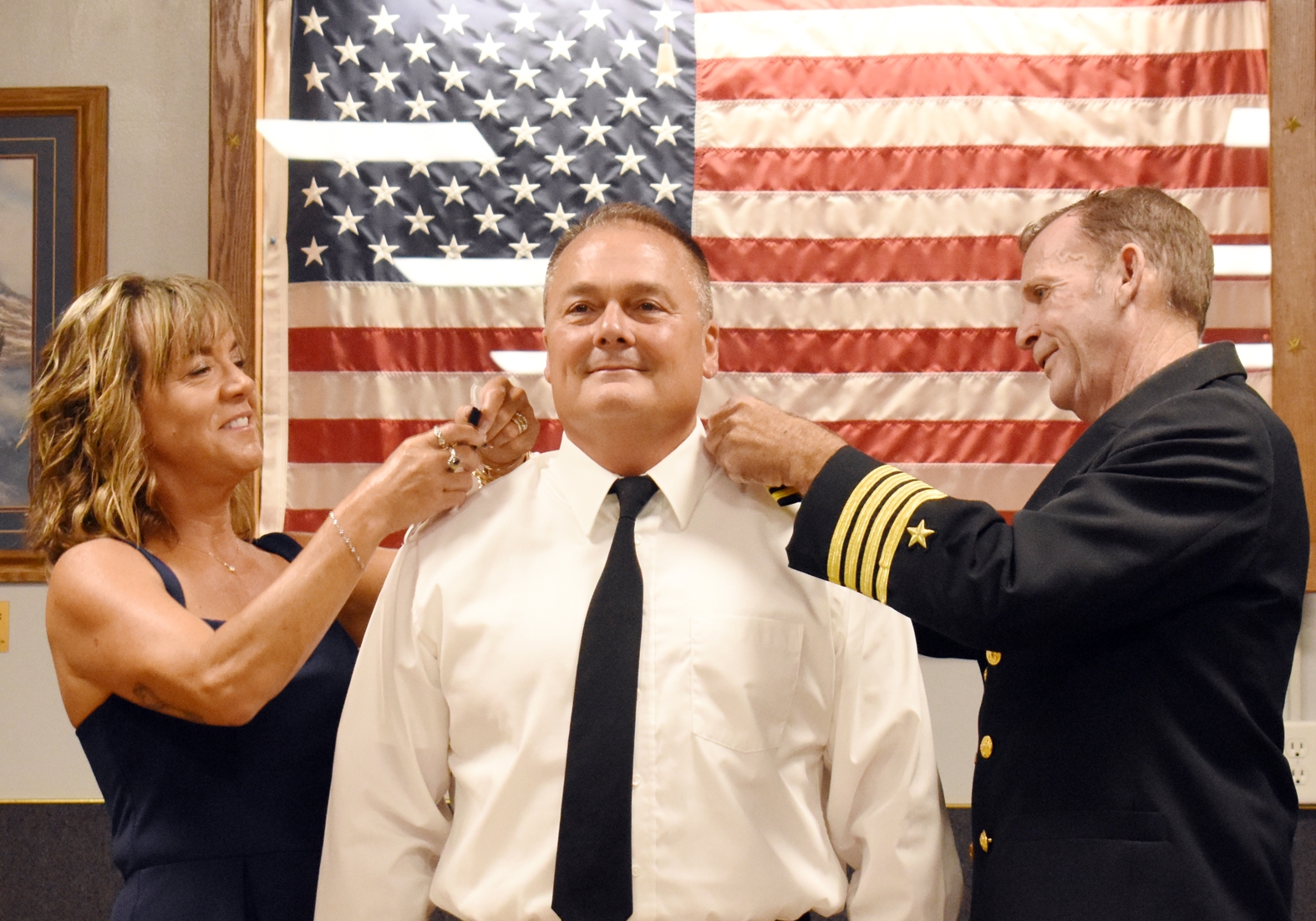 Tiffany Vikdal (left) and Capt. Dean Miereau (right) attach stripes to the uniform of Monty Vikdal, signifying his new rank of captain in the US Navy Reserve.